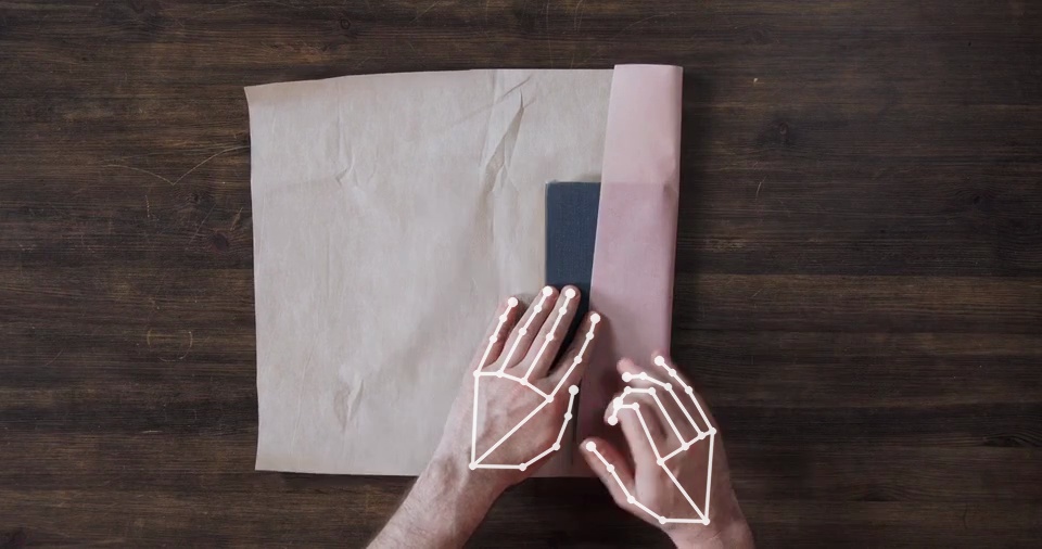 First-person view of hands wrapping a notebook, both hands tracked joint by joint by the Handtrace engine.